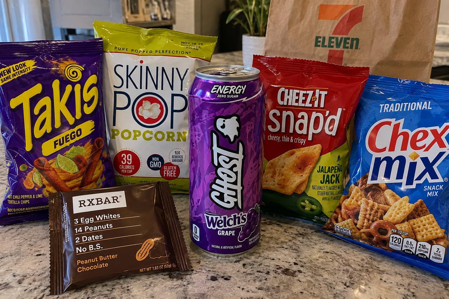 GHOST Welch’s Grape energy drink surrounded by Takis Fuego, SkinnyPop, Cheez-It Snap’d, Chex Mix and an RXBAR on a kitchen counter
